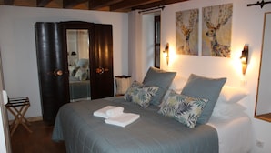 Una cama bien hecha con cubrecama azul y almohadas blancas, un armario de madera oscura y dos lámparas de pared.