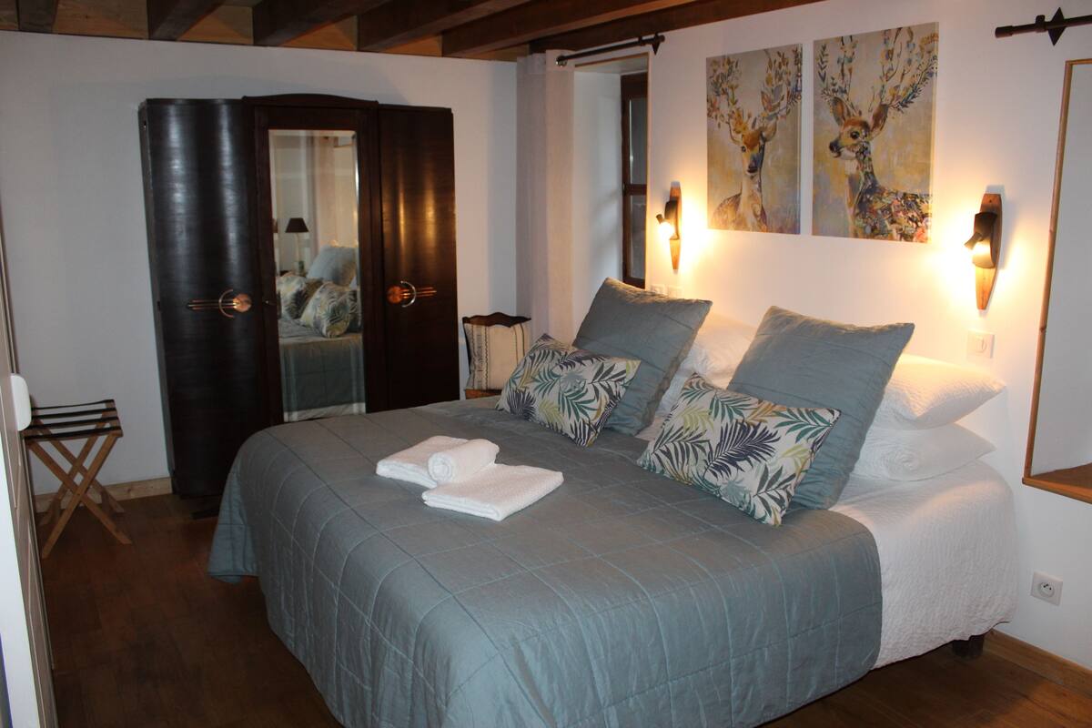 Een opgemaakt bed met een blauwe spreidek en witte kussens, een donkere houten garderobe en twee wandlampen.