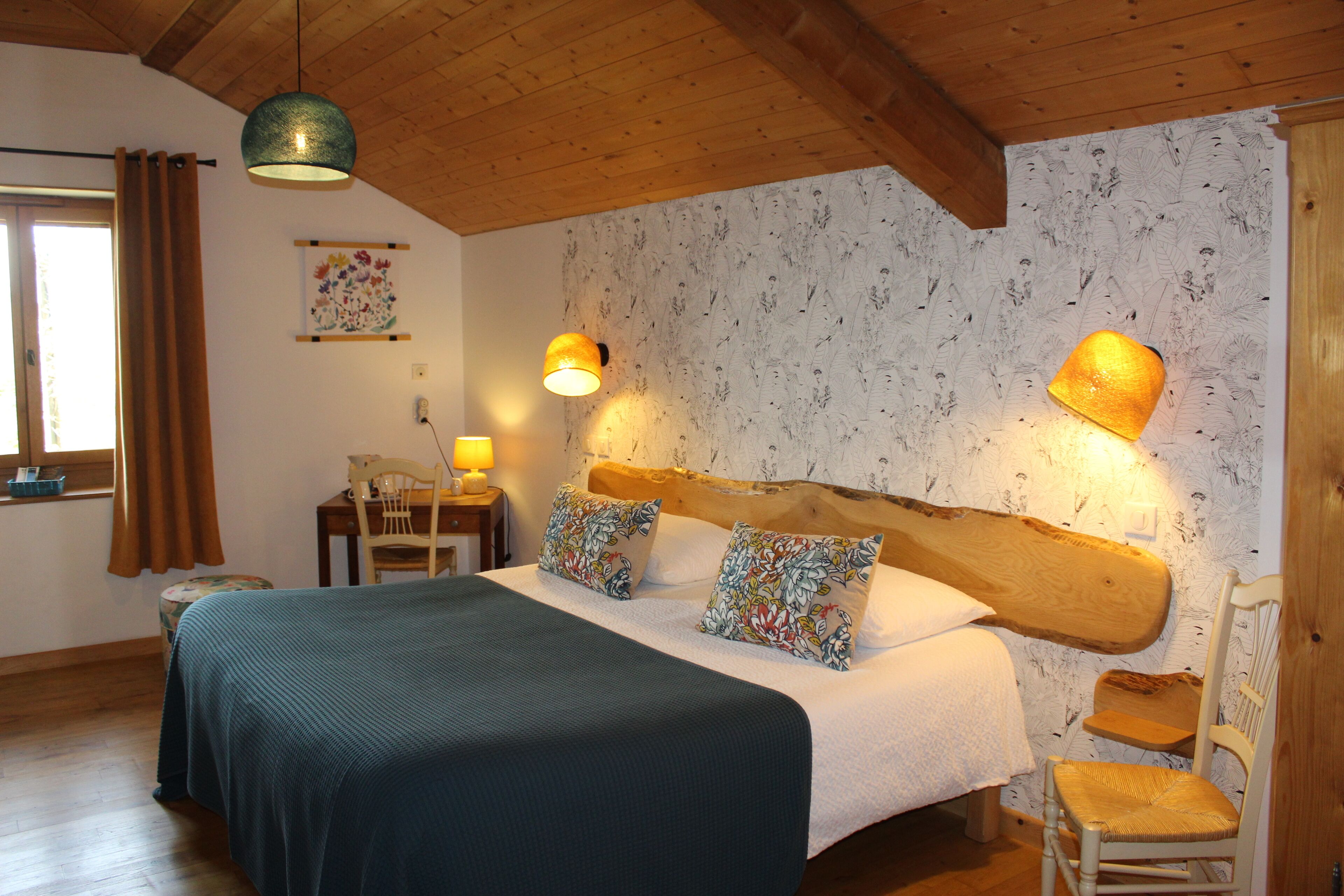 Ein Schlafzimmer mit einem hölzernen Kopfende, einem Bett mit grüner Bettdecke, zwei Nachttischlampen, einem Stuhl und einem kleinen Tisch mit einer Lampe.