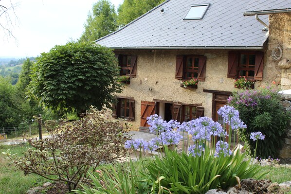 A rustic stone house with wooden shutters, a sloped roof, and a garden with purple flowers. - Les Pipistrelles (Saint-Beron)