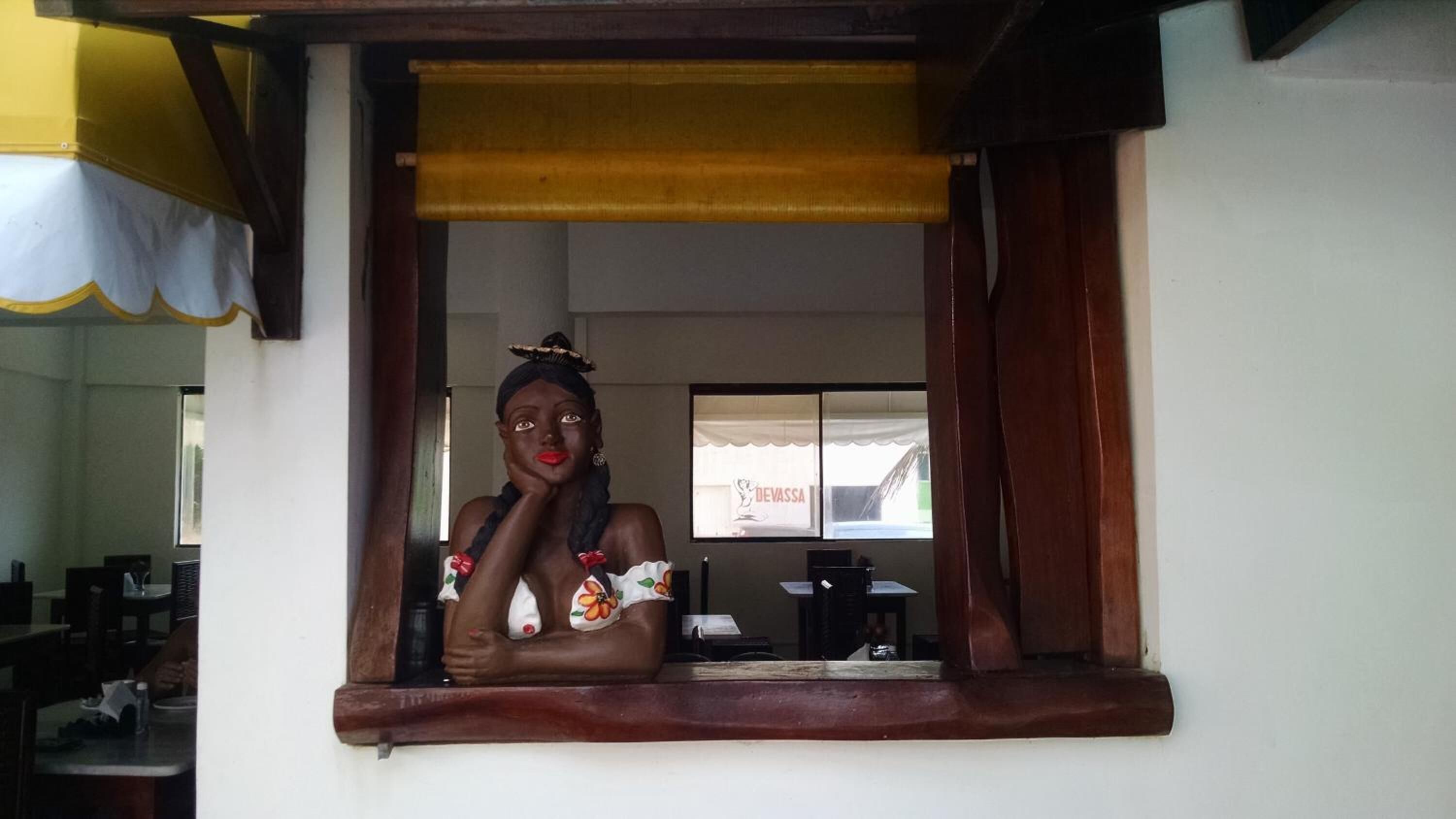 A person standing in a window with a view of a room that includes a table and chairs.