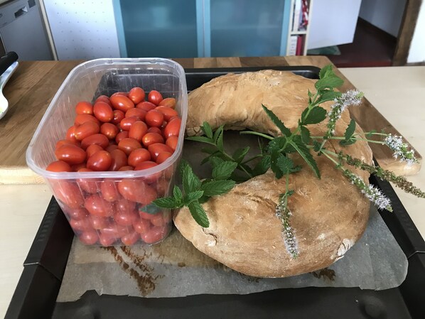 A kitchen counter with a plastic container of cherry tomatoes, a loaf of bread, and fresh mint leaves. - Calme et Nature (Saint Sever)
