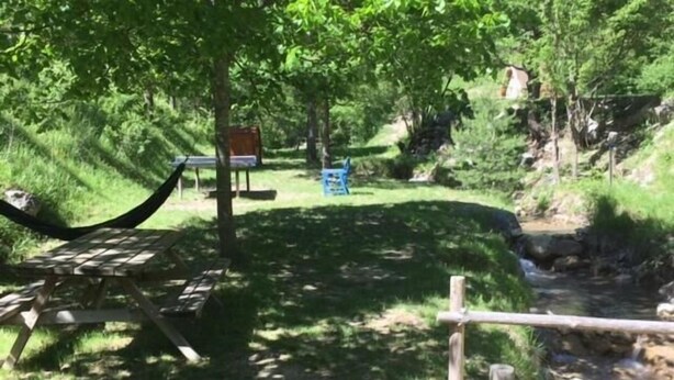 A picnic area with a hammock, a bench, and a table, surrounded by greenery and a small stream. - Calme et Nature (Saint Sever)
