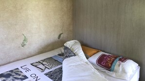 A small, compact room with a bed, a green shelf, and a wall with a textured finish. - Calme et Nature (Saint Sever)