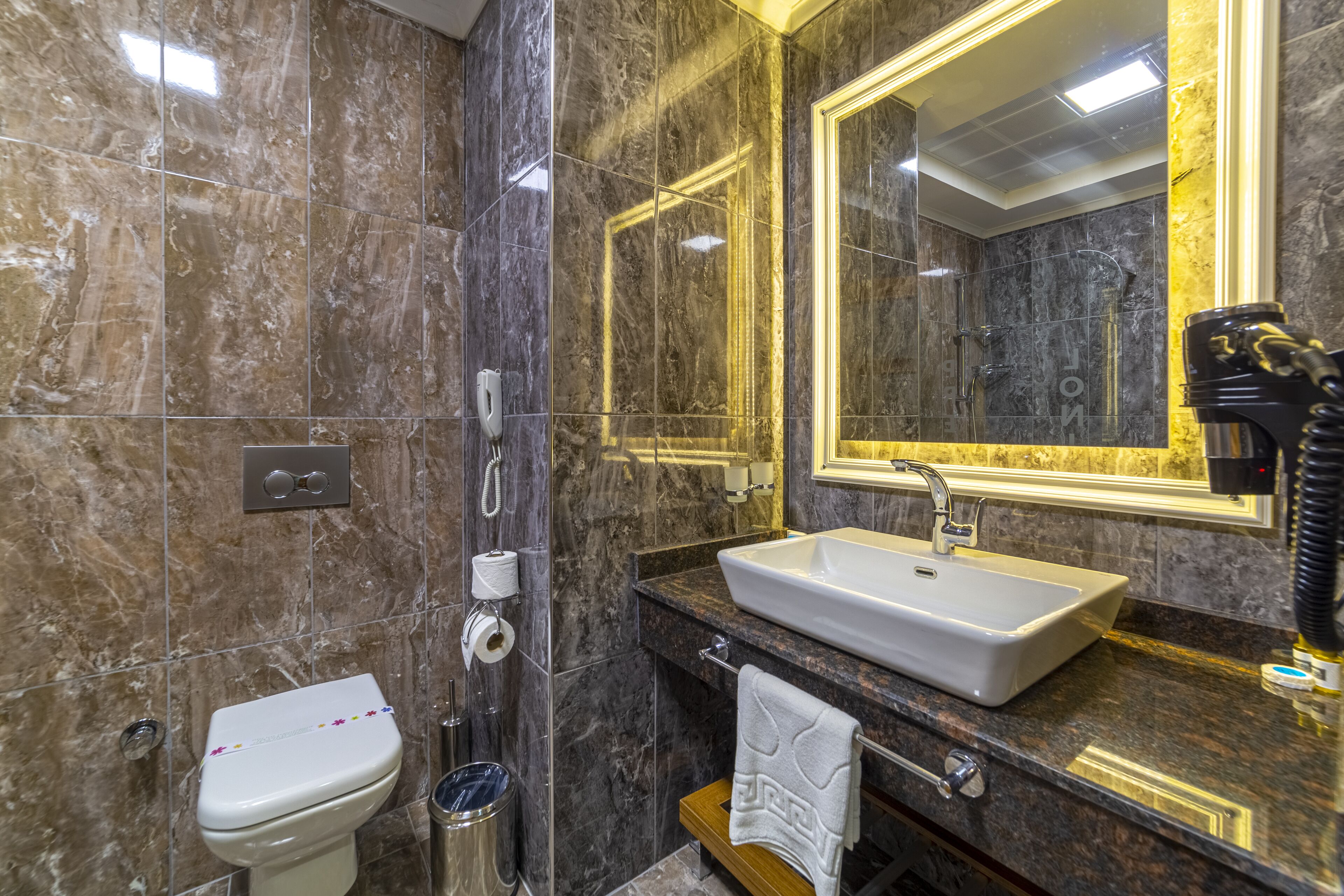 A bathroom with a marble floor, a white sink, a large mirror with a gold frame, a towel rack, and a toilet.