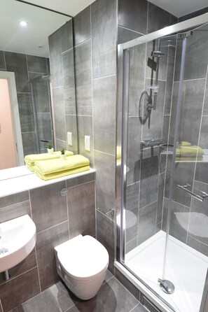 A modern bathroom with a glass-enclosed shower, a white toilet, and a sink with a yellow towel on the counter.