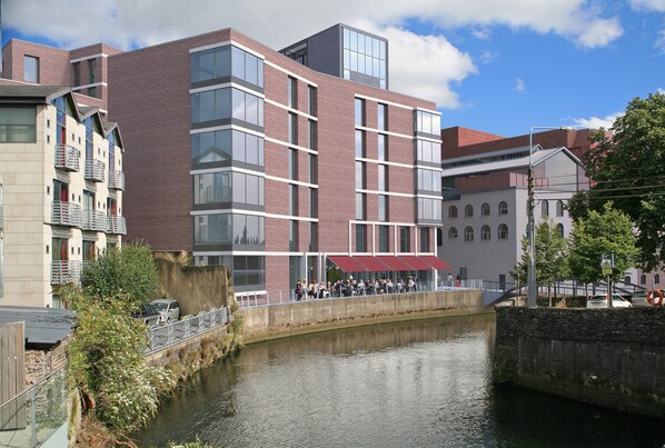A modern building with multiple windows and balconies, a canal in front, and a pedestrian bridge.