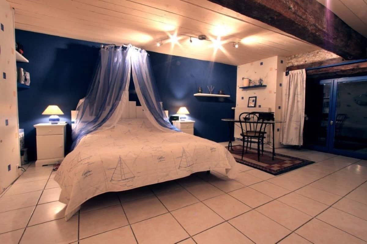 A bedroom with a canopy bed, two bedside tables with lamps, a chair, and a view of the outside through a glass door.