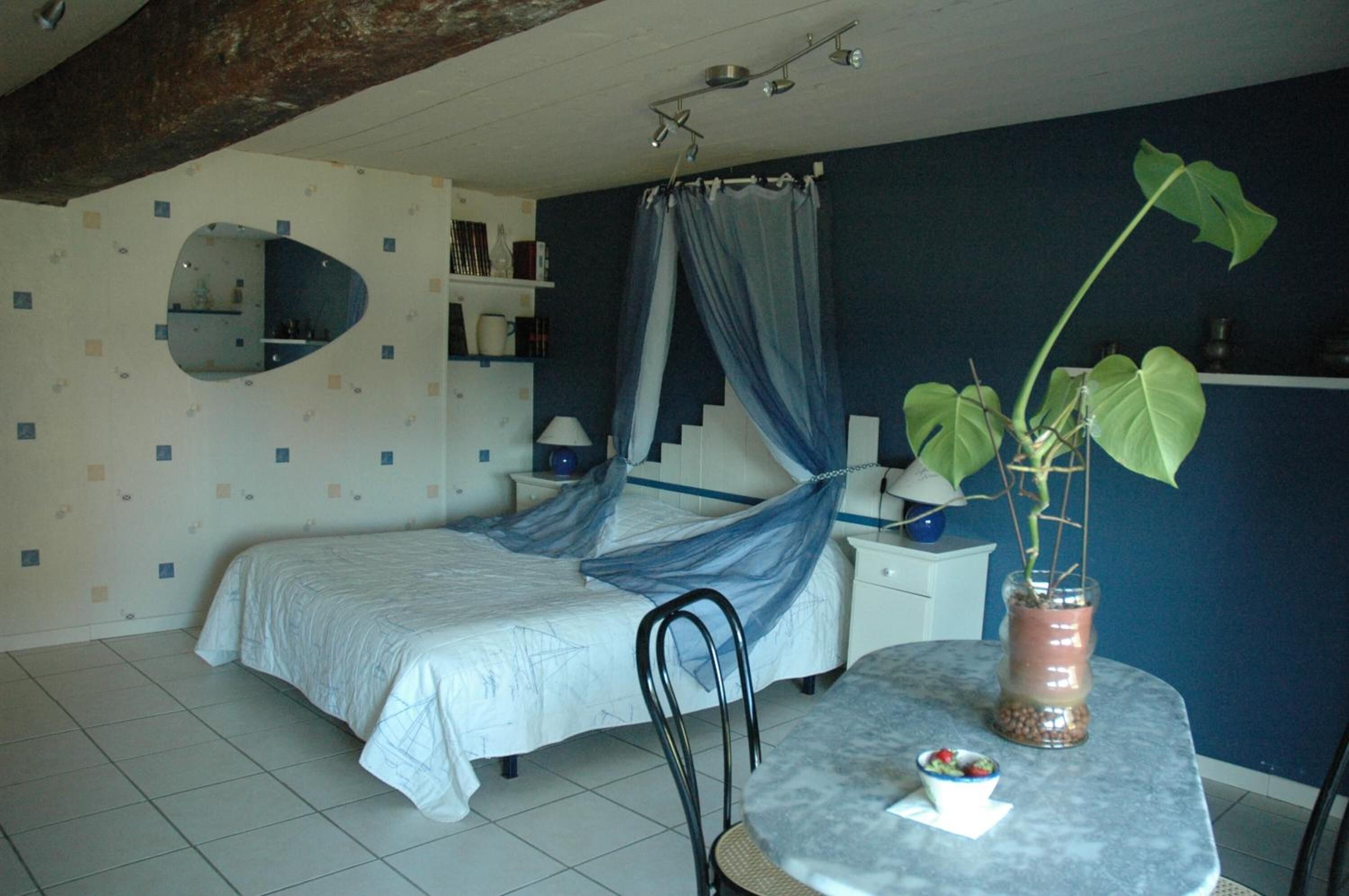 Un dormitorio con una cama, una mesa con una planta, una silla, un espejo y una escalera.