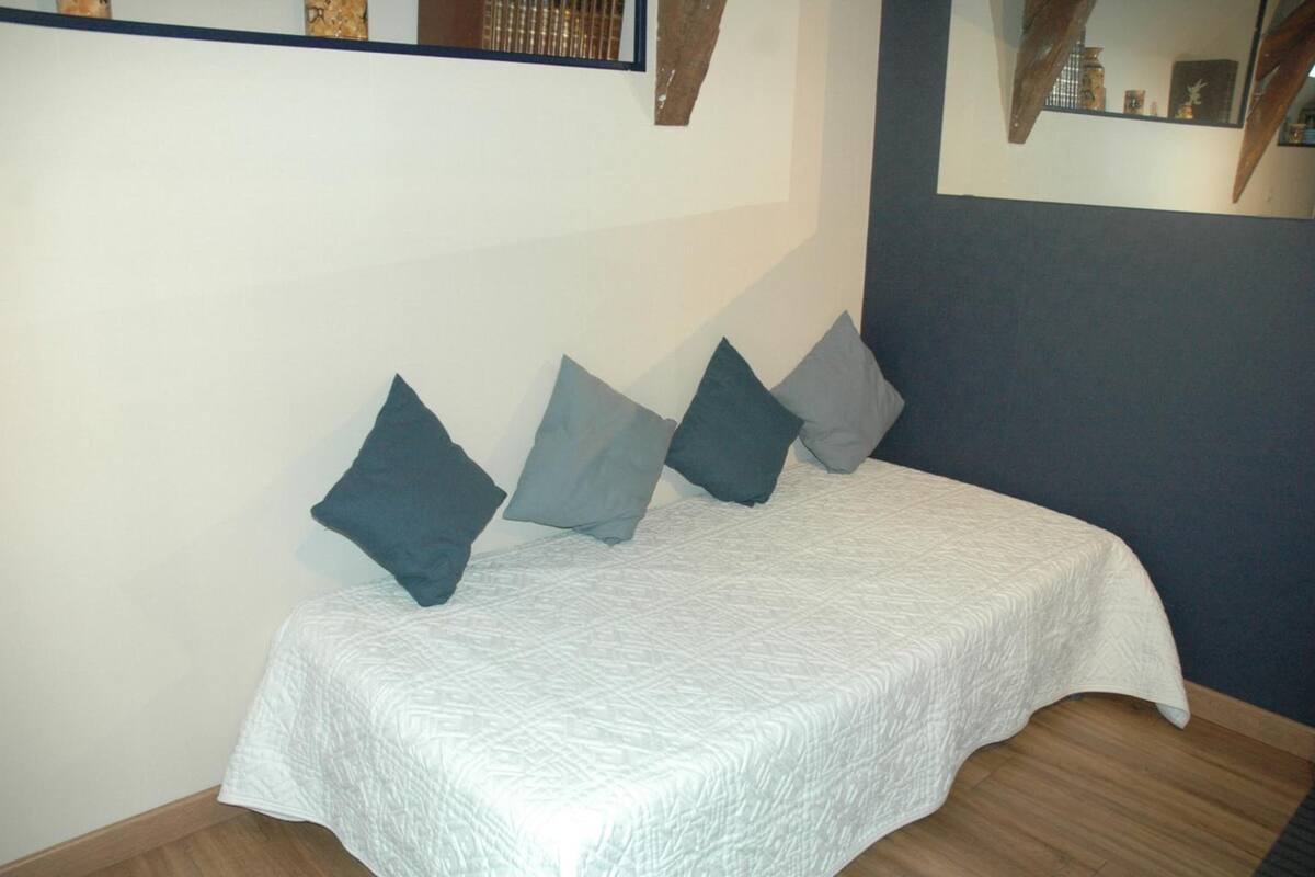 A bed with a white quilt and four pillows in shades of blue and gray.