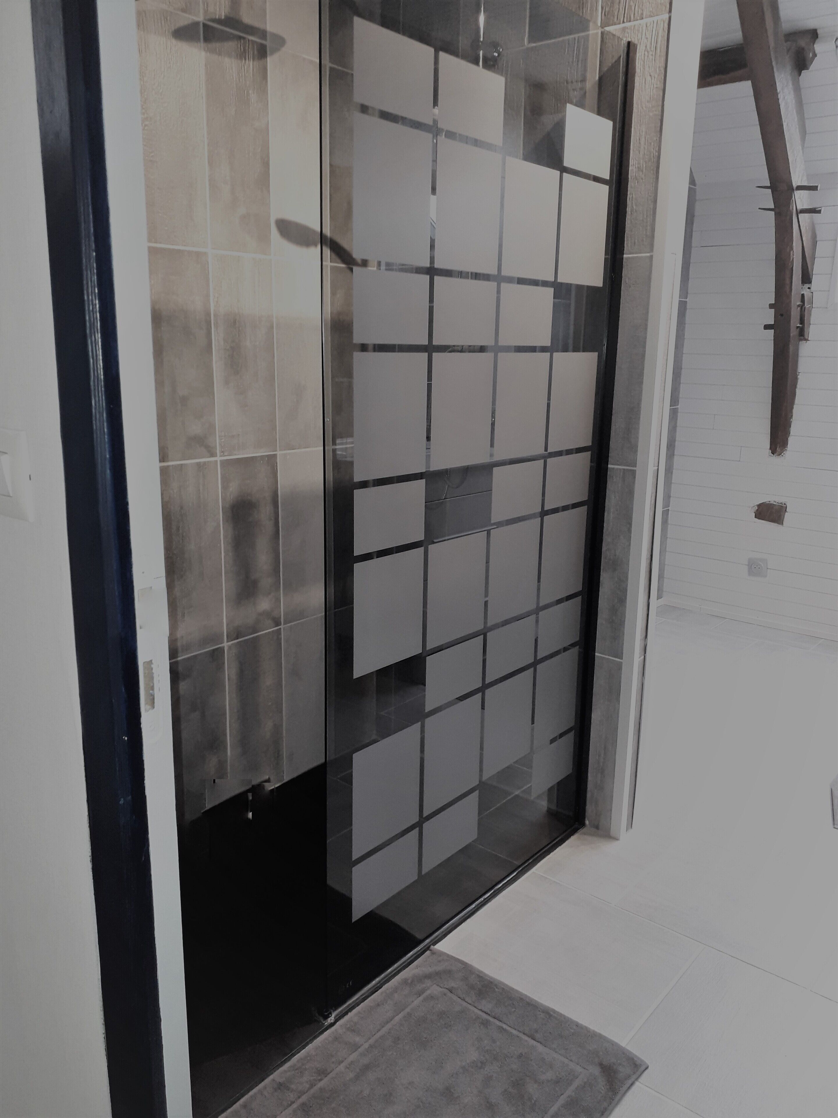 Une salle de bain moderne avec une douche à l’italienne en verre, des murs carrelés et une pomme de douche visible.