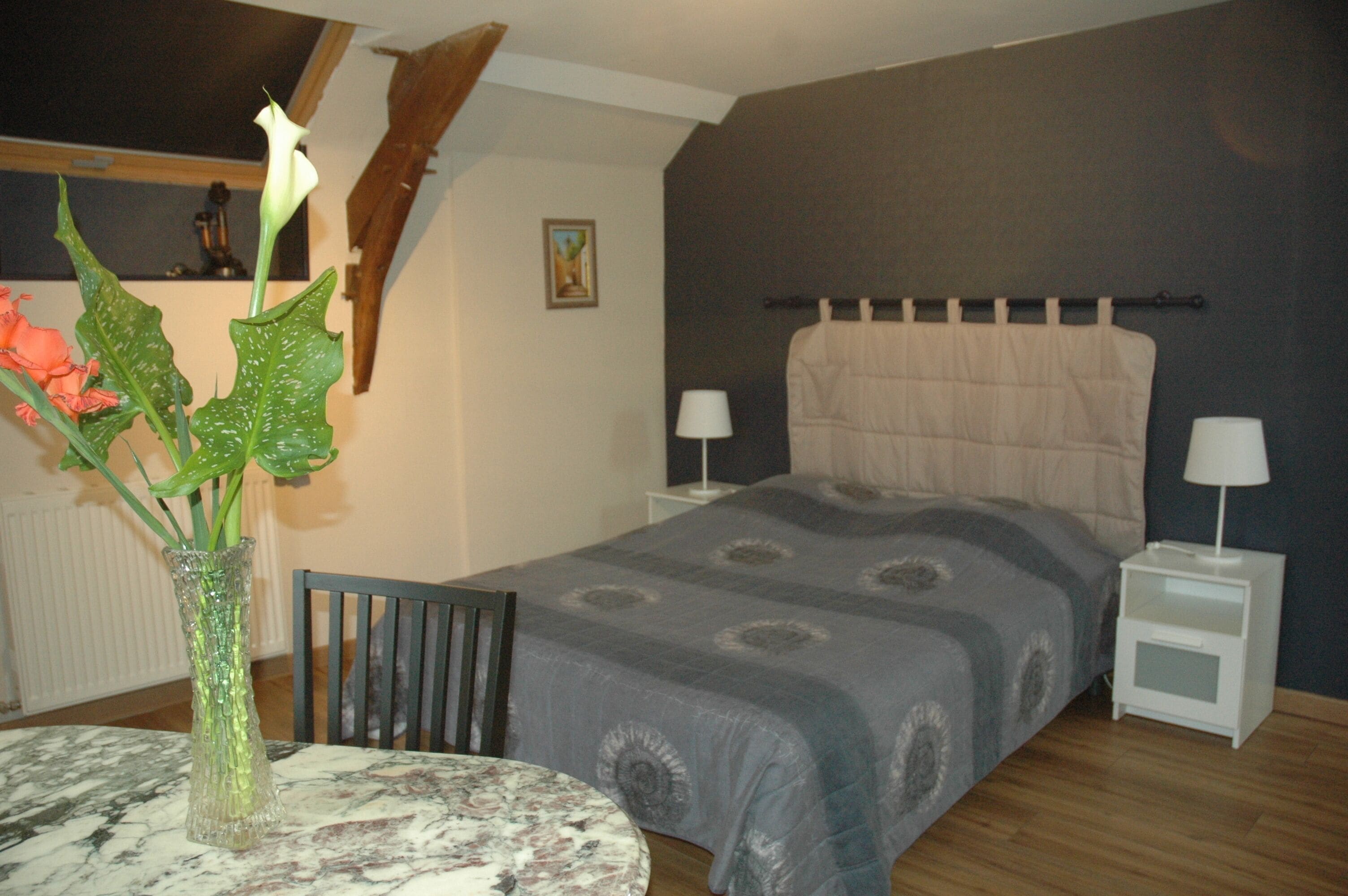 A bedroom with a bed, nightstands, a table with a vase, and a chair.