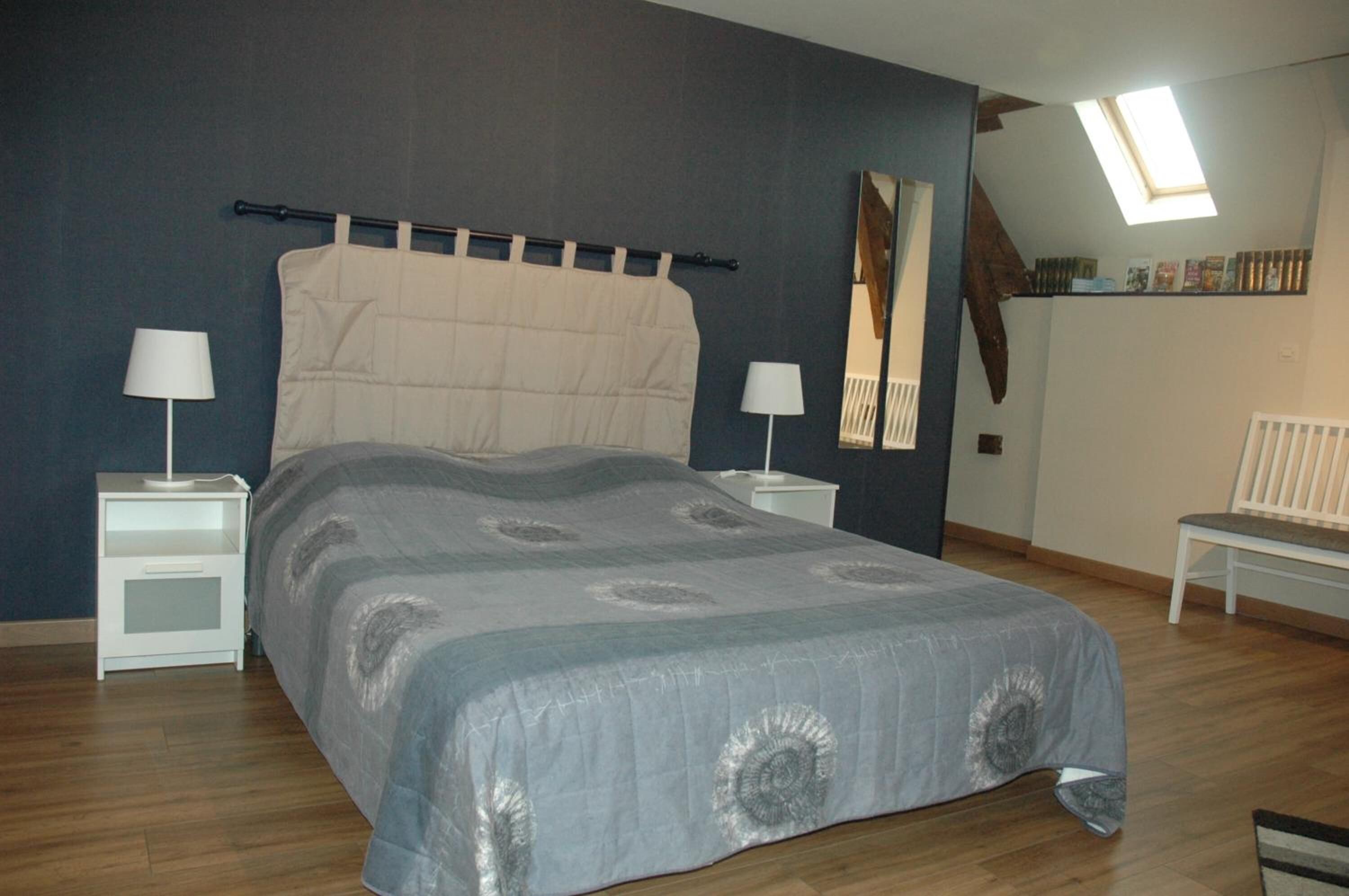 Una camera da letto con un letto, due comodini, una panca e un lucernario.