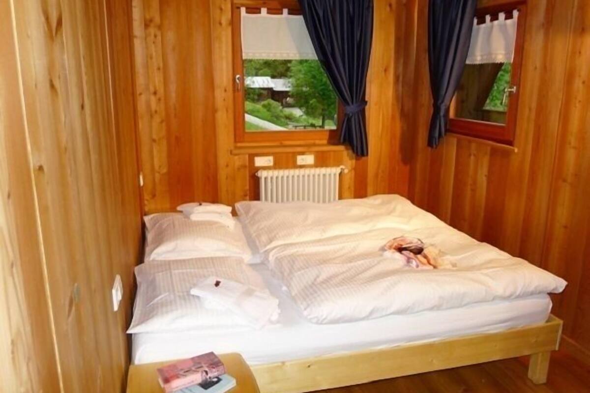 A wooden cabin room with a bed, a nightstand, and a window with curtains.