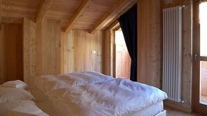 A wooden cabin bedroom with a bed, a window, and a radiator.