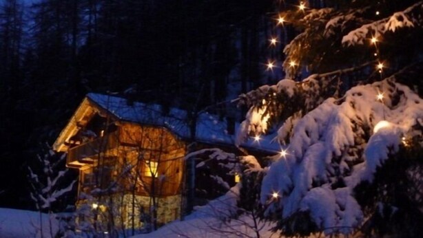 A cozy cabin with a warm glow, surrounded by snow-covered trees and a clear night sky.