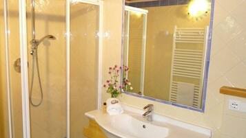 A bathroom with a glass-enclosed shower, a sink with a mirror above it, and a vase with flowers on the vanity.