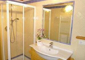 Un baño con ducha envuelta en vidrio, un lavabo con espejo y un florero con flores sobre el mueble.