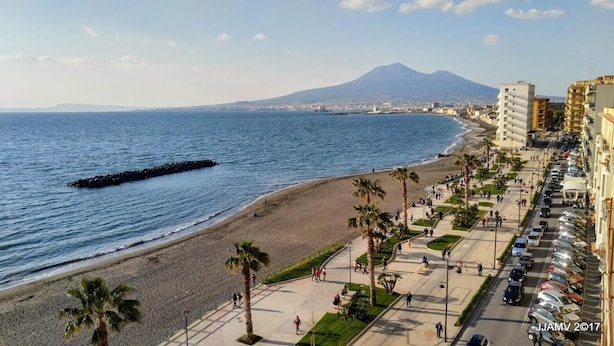 Un paisaje costero con playa, palmeras y una montaña al fondo.