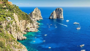 Un paisaje costero con acantilados rocosos y aguas azules cristalinas. Se ven barcos en el mar.