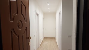 Un pasillo con suelo de madera, paredes blancas y una puerta marrón con pomo circular.