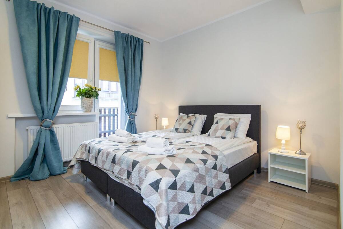 A modern bedroom with a bed, curtains, a nightstand, and a lamp.