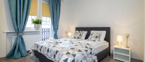 Un dormitorio moderno con cama, cortinas, una mesita de noche y una lámpara.