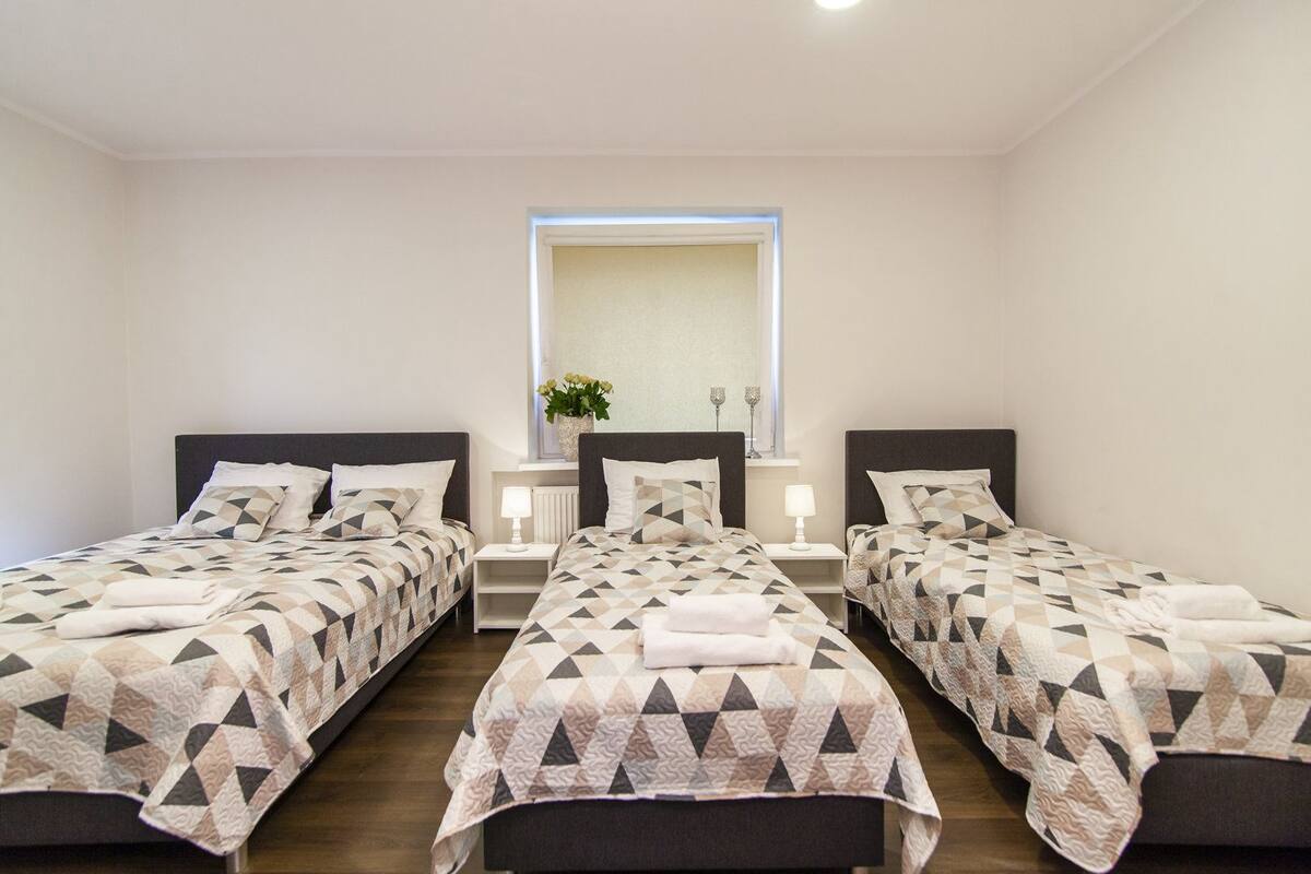 A room with two beds, each with a geometric-patterned bedspread, a bedside table with a lamp, and a mirror above the beds.