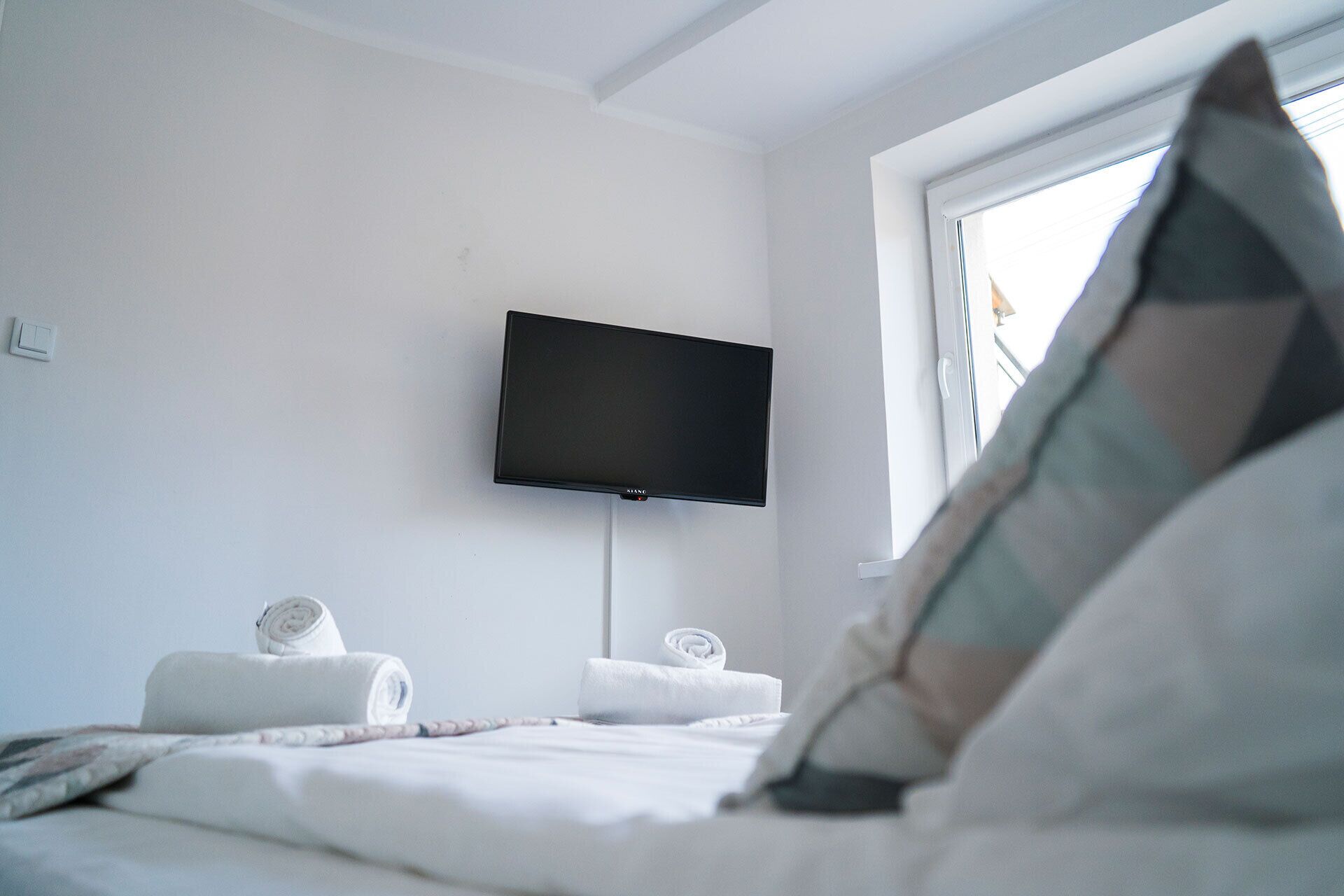 A hotel room with a bed, a flat-screen TV mounted on the wall, and a window with a view of the outside.