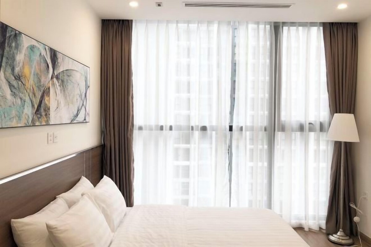 A hotel room with a large bed, a painting on the wall, and a window with curtains.