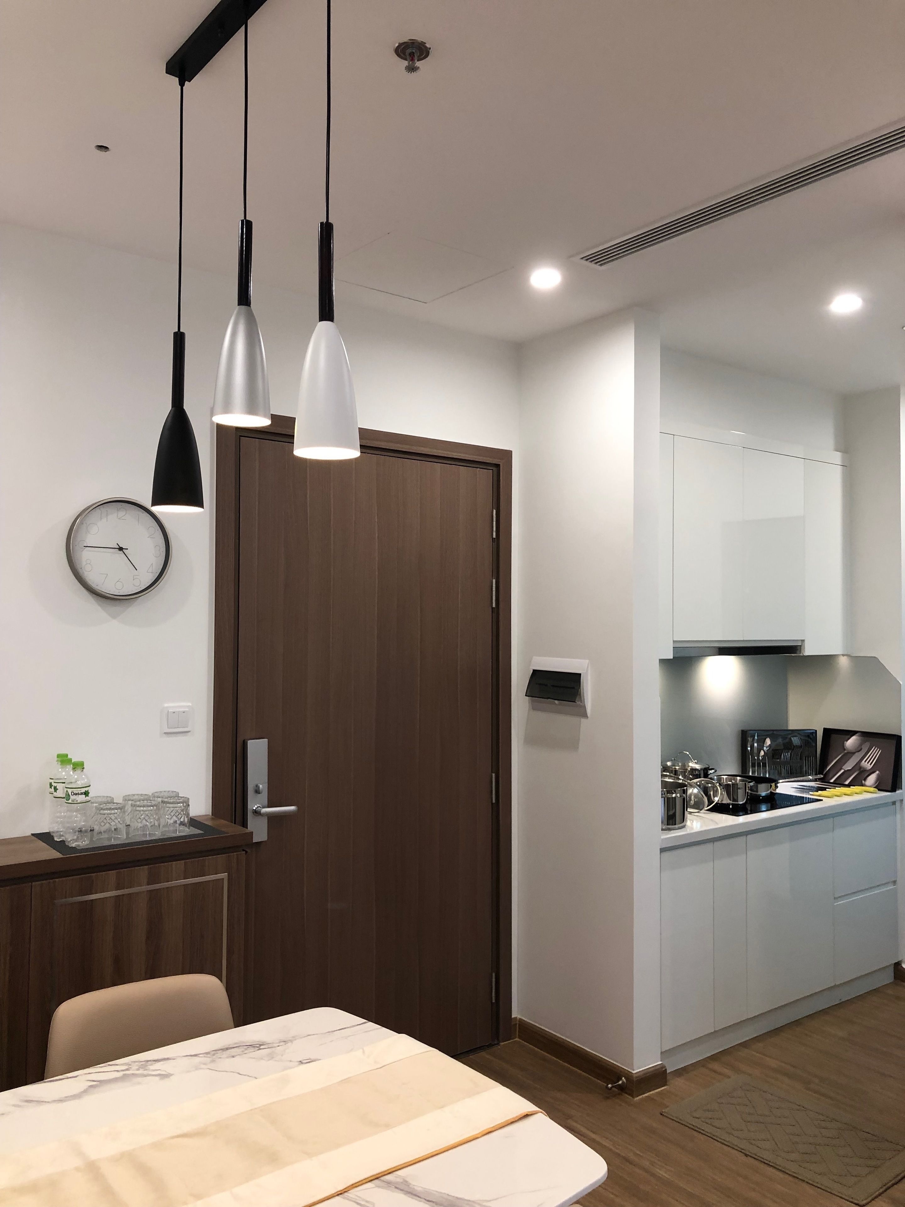 Eine moderne Küche mit weißen Schränken, einem eingebauten Ofen und einer Edelstahl Arbeitsplatte. Ein Essbereich mit einem Marmortisch und zwei Pendelleuchten darüber.