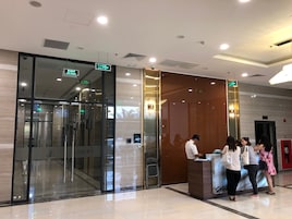 Zona de recepción de un hotel con entrada de vidrio, un mostrador de recepción y una pantalla informativa digital.