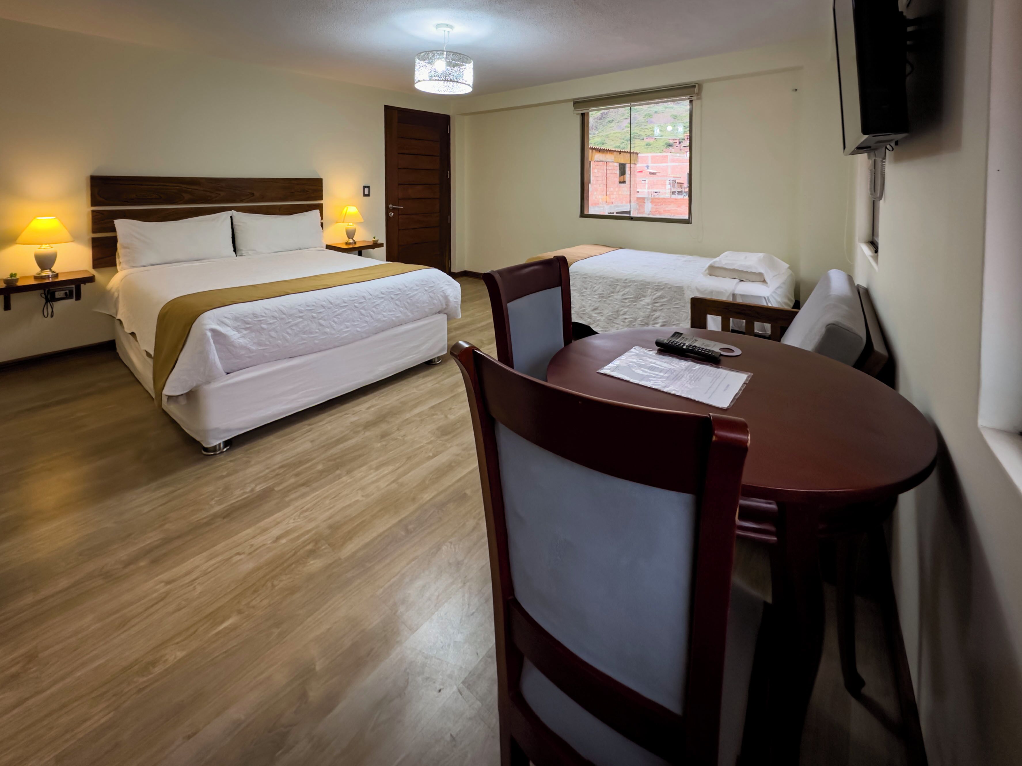 A hotel room with a bed, a desk, a chair, a lamp, a TV, and a window.