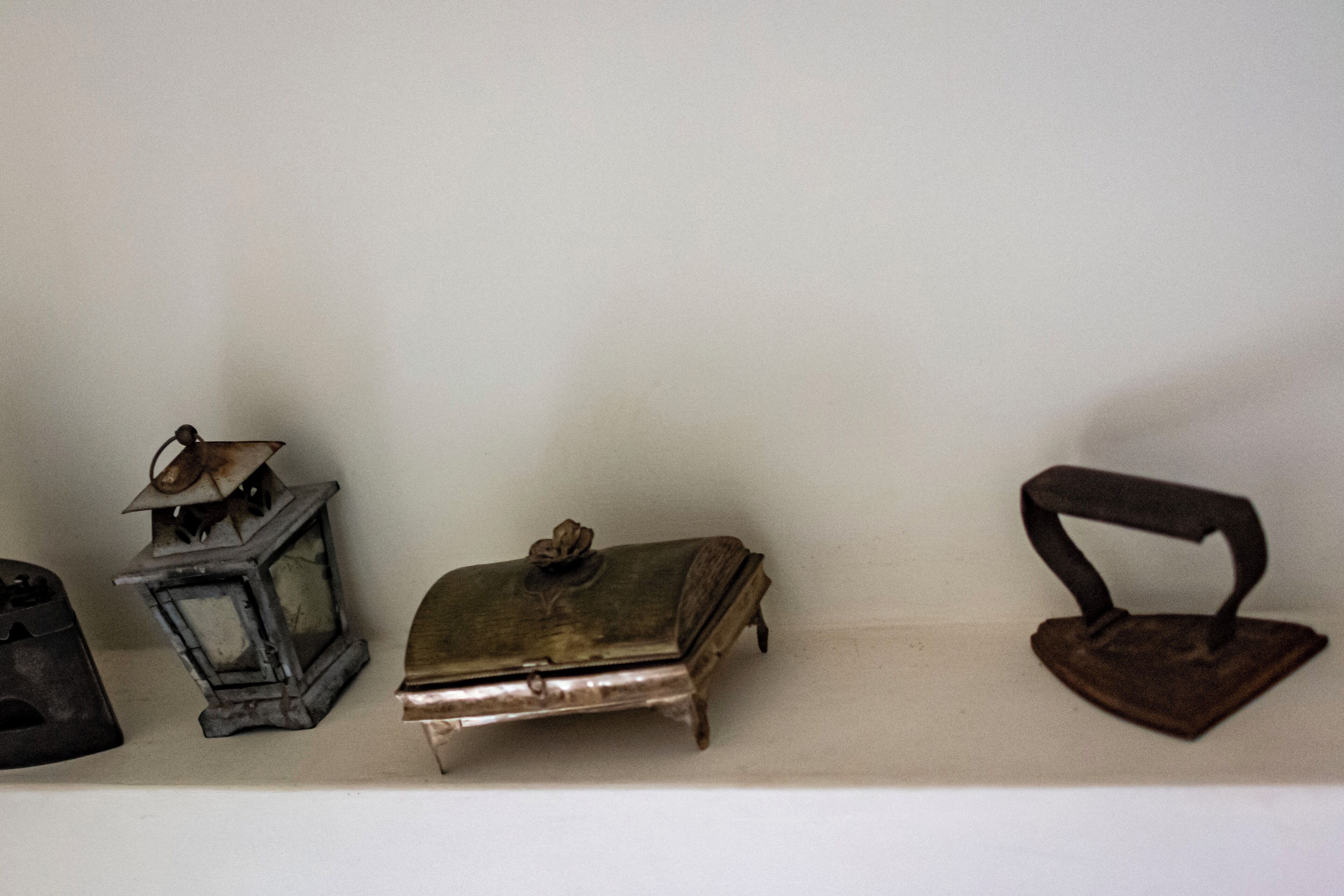 Une étagère sur laquelle sont posés trois objets anciens : une lanterne, une petite boîte et un fer à repasser.