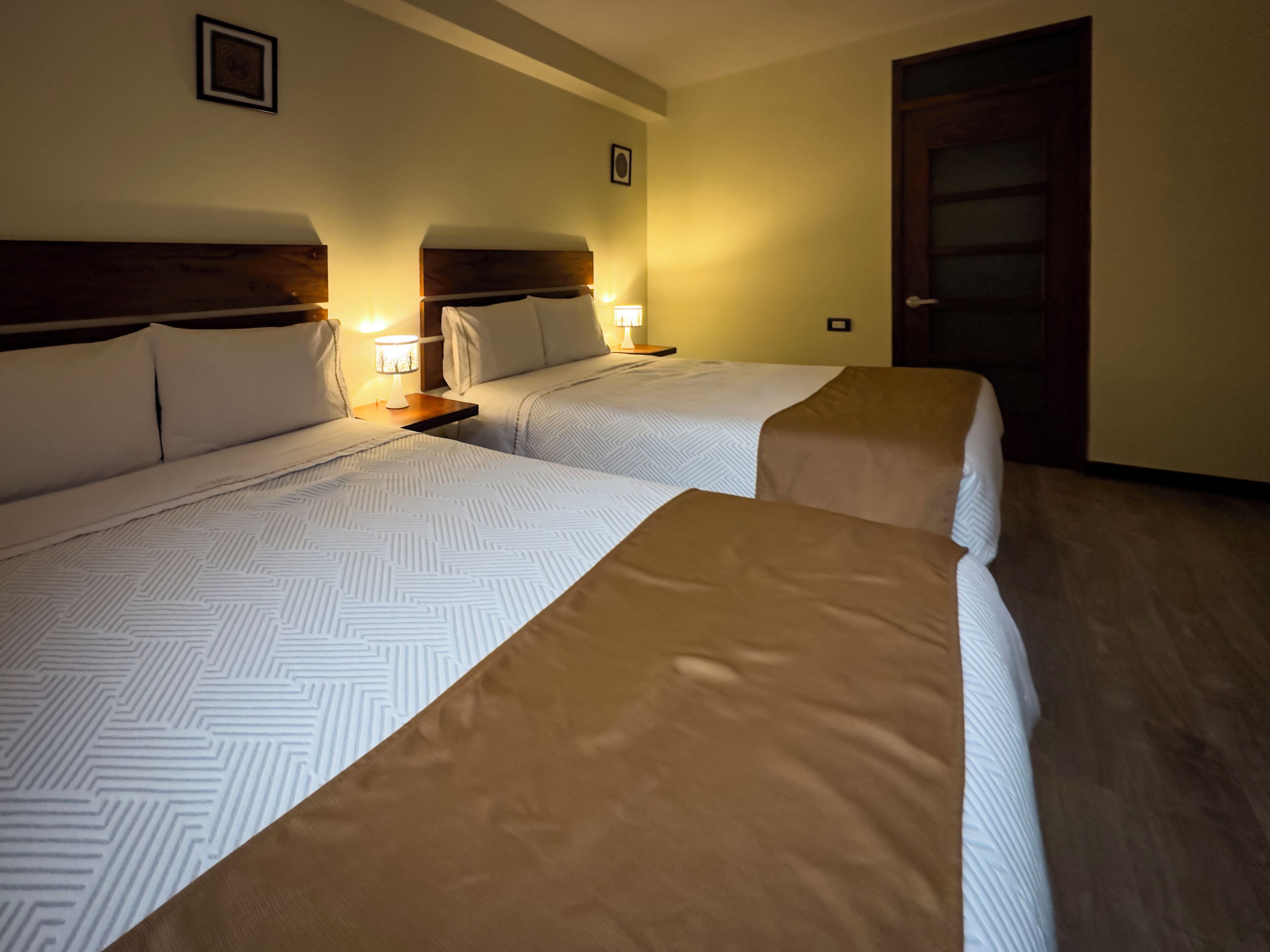 A hotel room with two beds, nightstands, and a door.