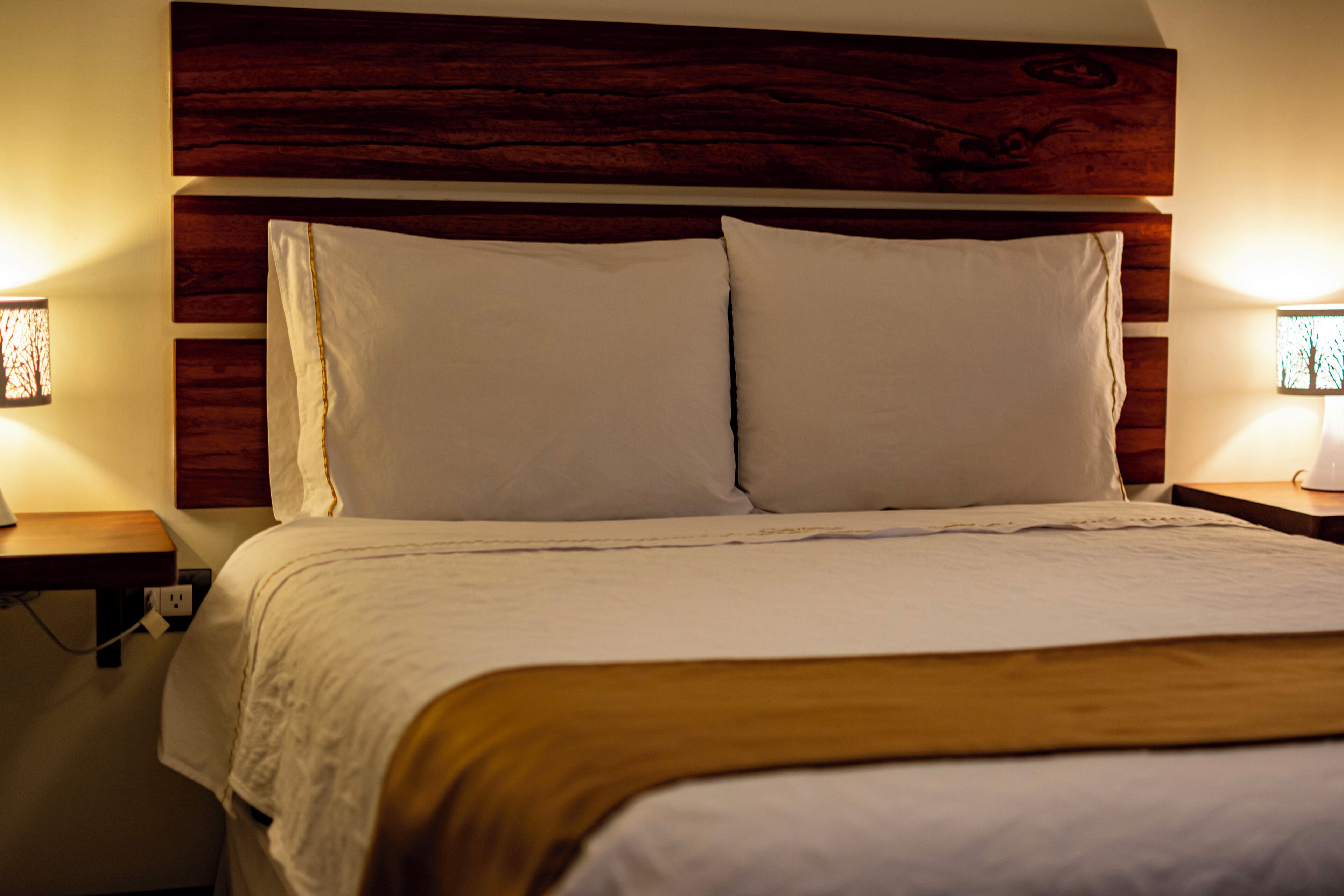 Una cama con ropa de cama blanca, un cabecero de madera y dos lámparas de noche.