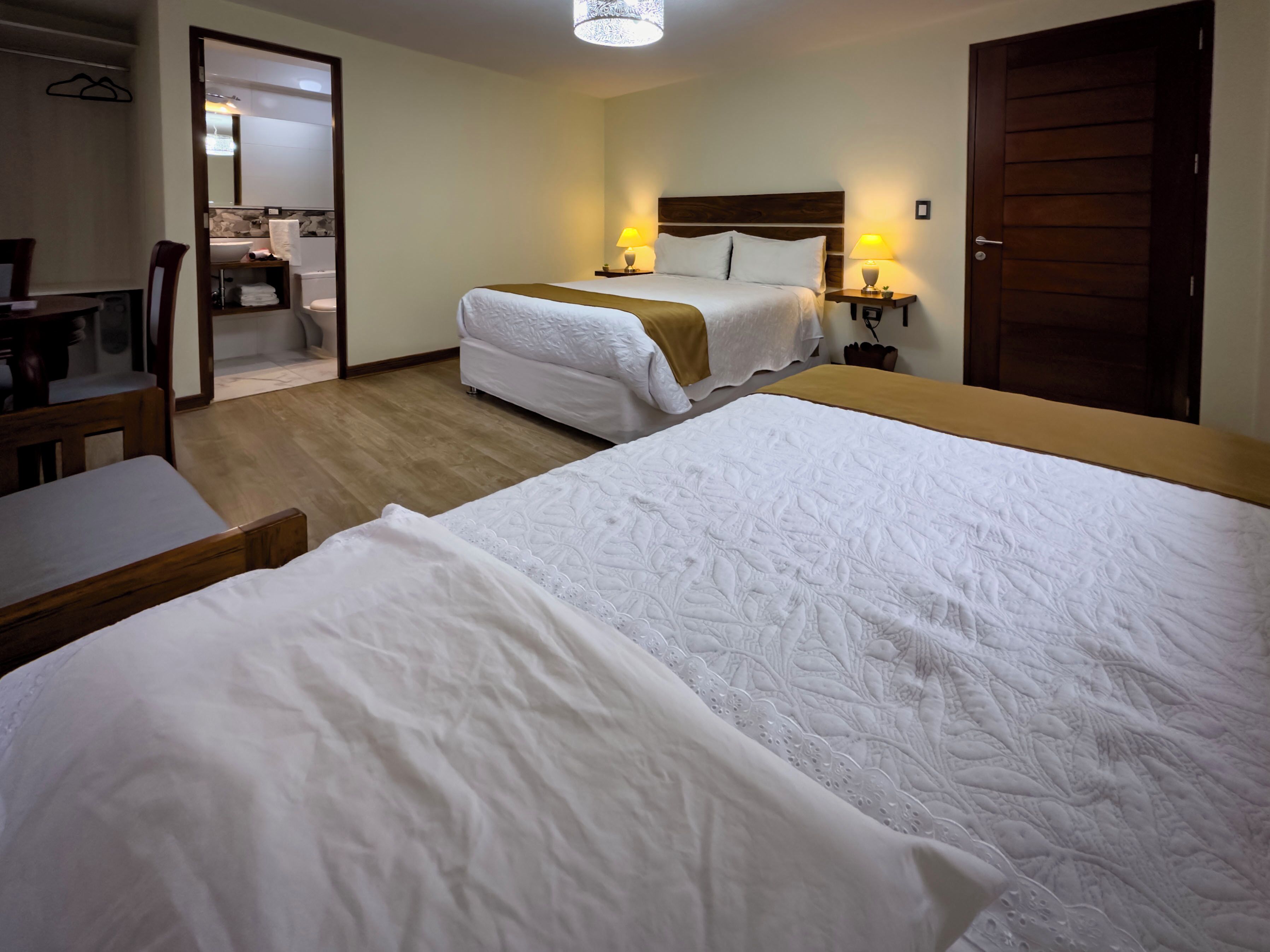 A hotel room with two beds, a desk, a chair, a bathroom, and a wooden door.