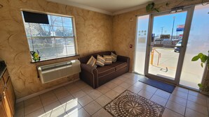 A reception area with a brown sofa, a window, a door, and a patterned rug. - Benbrook Inn & Suites (Fort Worth)