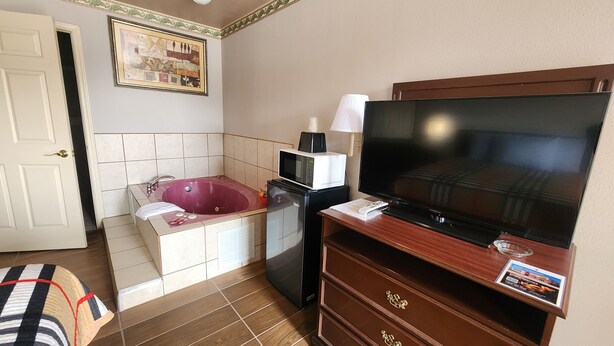 A bathroom with a bathtub, a microwave, a refrigerator, a television, and a wooden cabinet. - Benbrook Inn & Suites (Fort Worth)