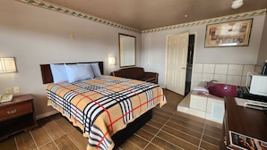 A hotel room with a bed, bedside table, nightstand, dresser, and a bathroom with a sink and mirror. - Benbrook Inn & Suites (Fort Worth)