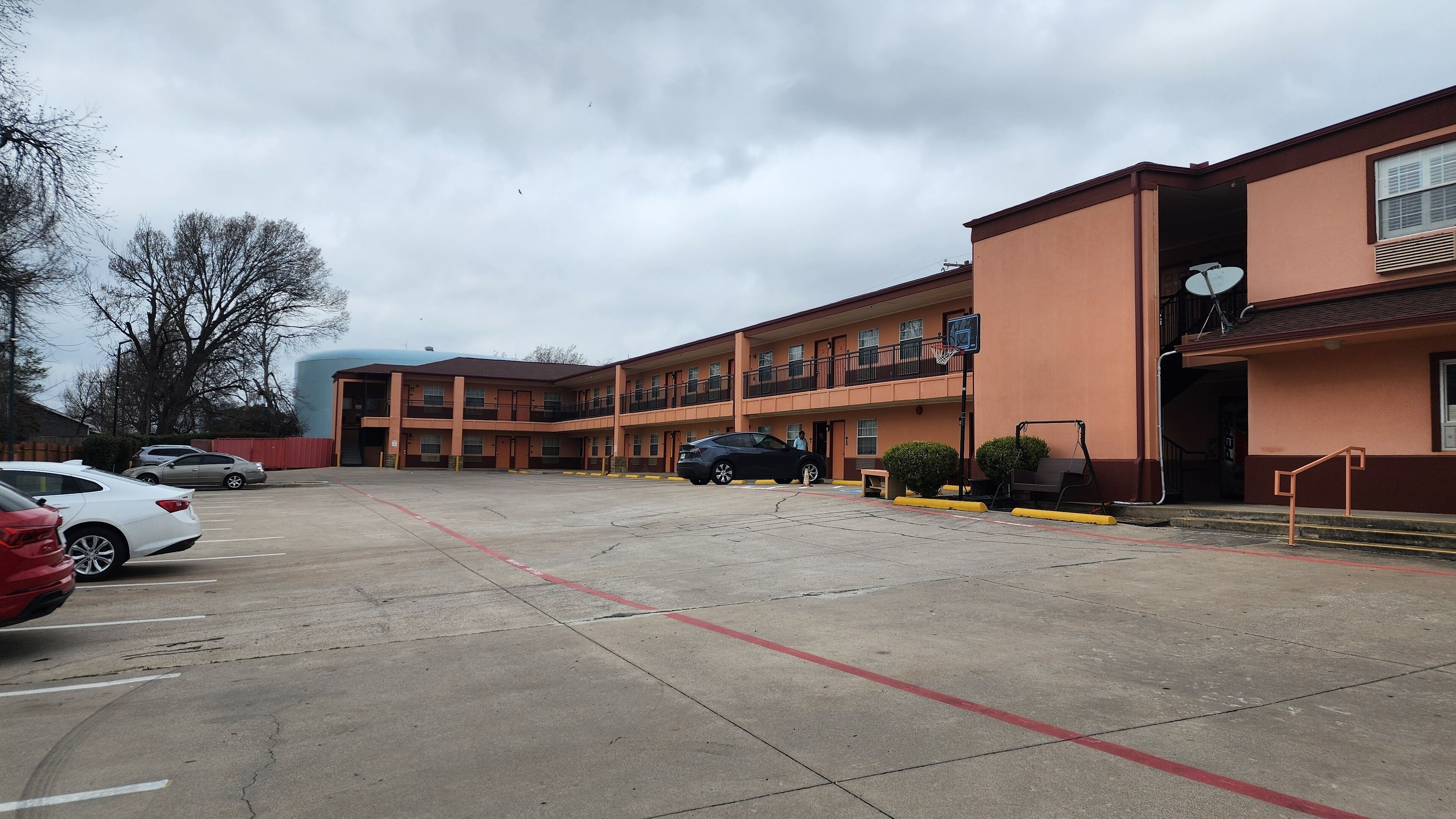 A multi-story motel with a parking lot, a basketball court, and a satellite dish on the roof.