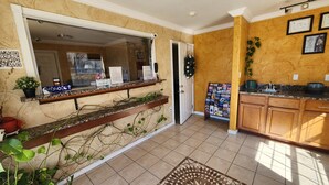 A kitchen with wooden cabinets, a tiled floor, a window with a view, and a door leading to another room. - Benbrook Inn & Suites (Fort Worth)