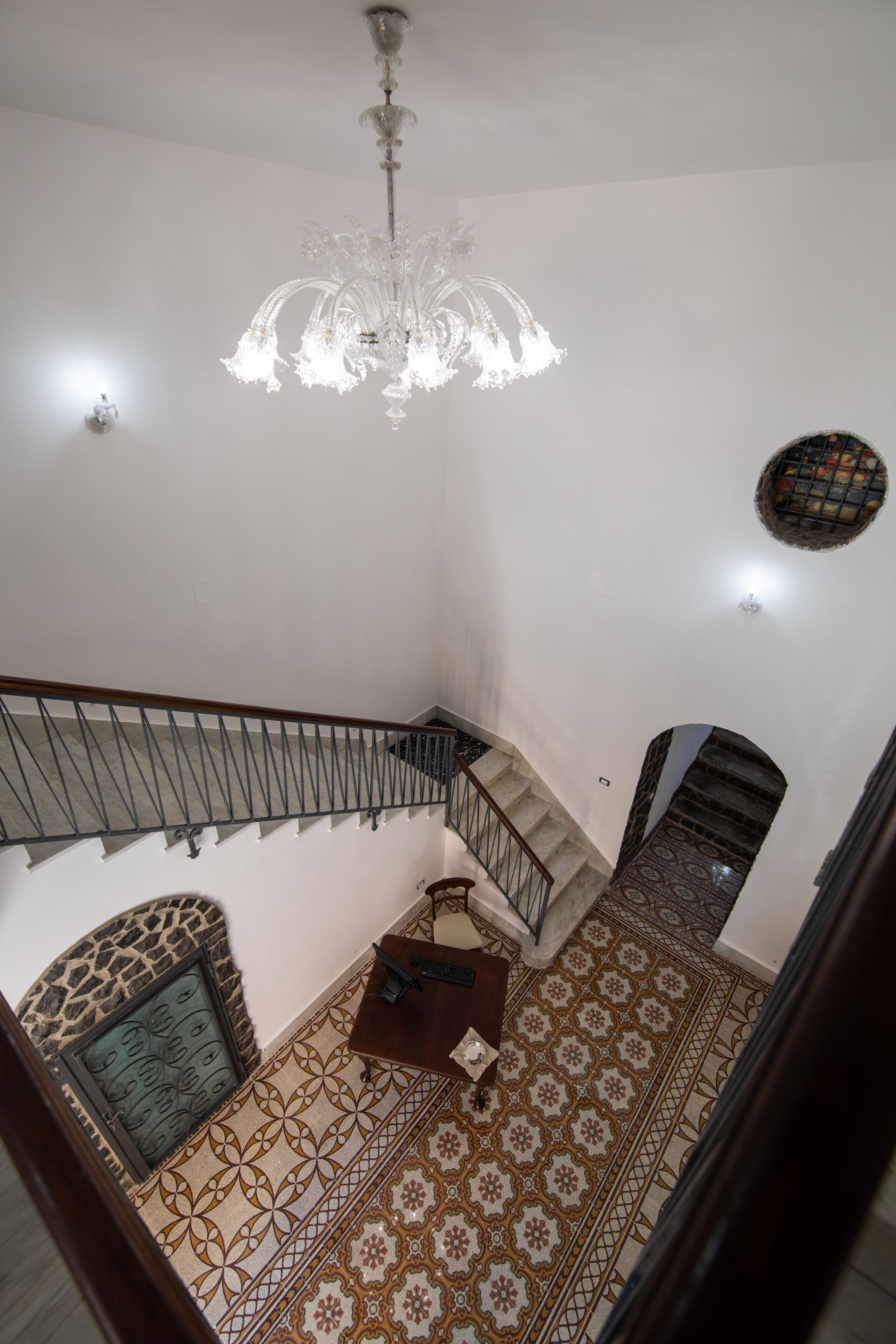 Una escalera con piso estampado, un candelabro y una lámpara de pared.