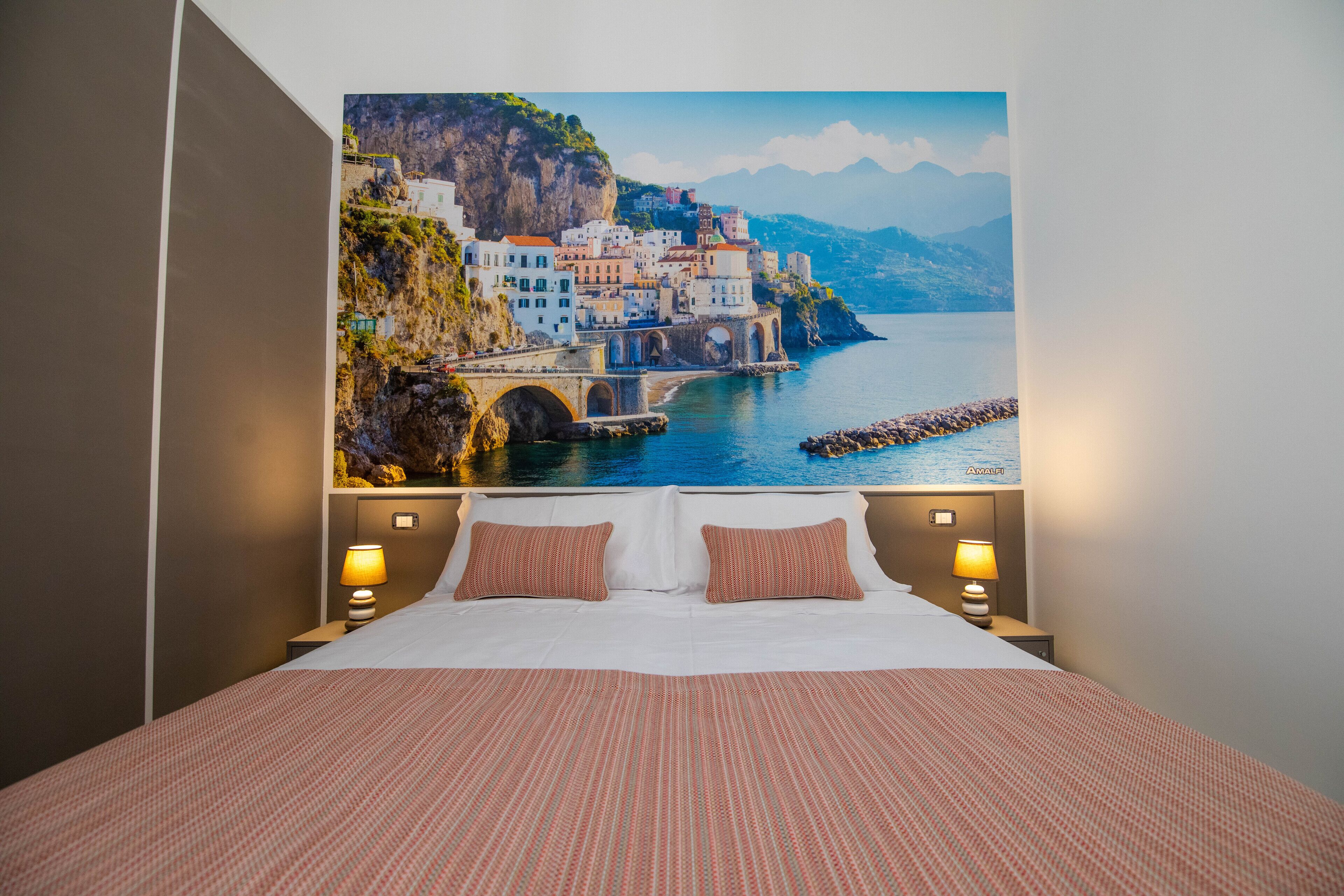 Une chambre d’hôtel avec un grand lit, deux lampes de chevet et une fresque représentant une ville côtière.