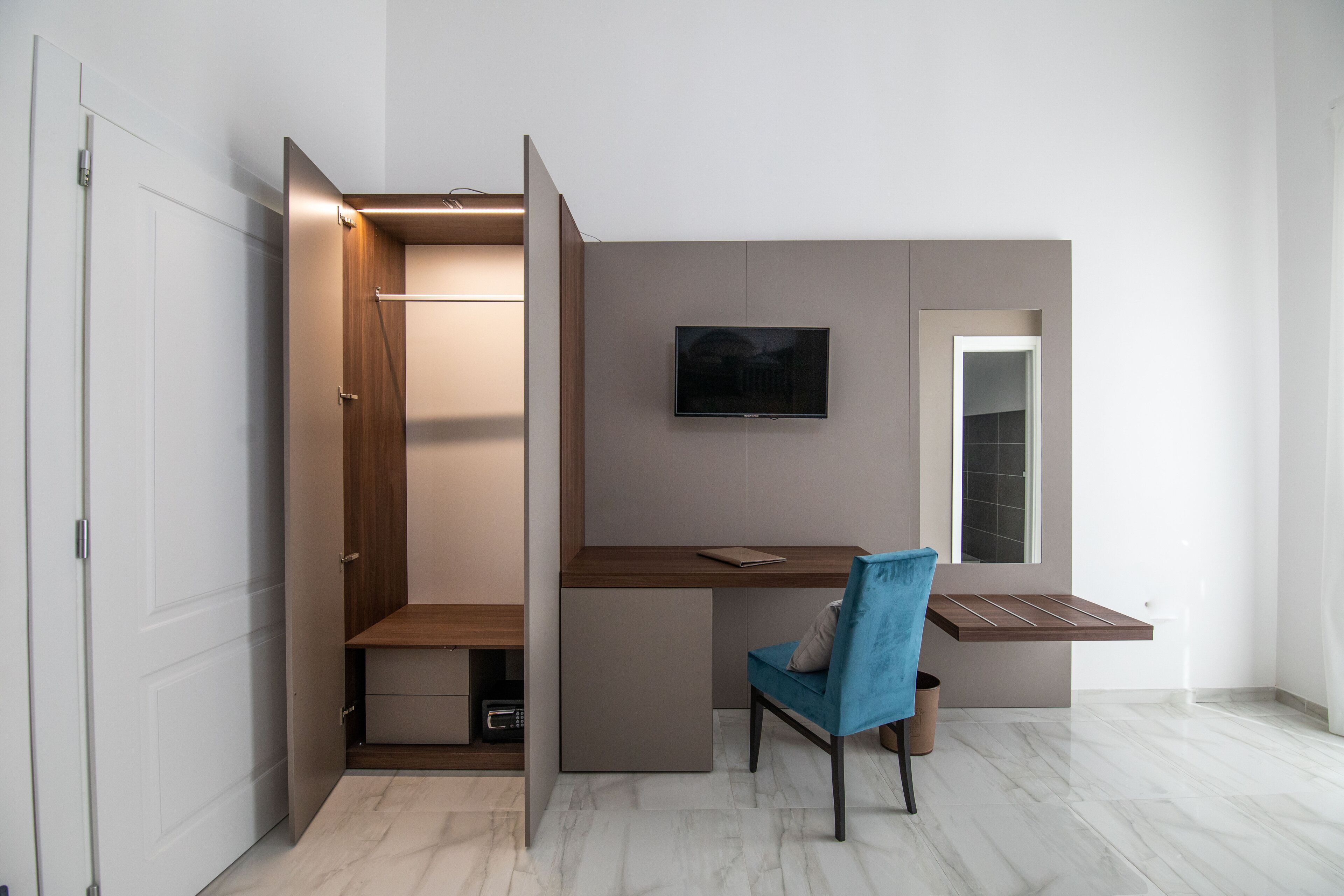 Quarto moderno com escrivaninha embutida, uma cadeira, televisão e guarda-roupa.