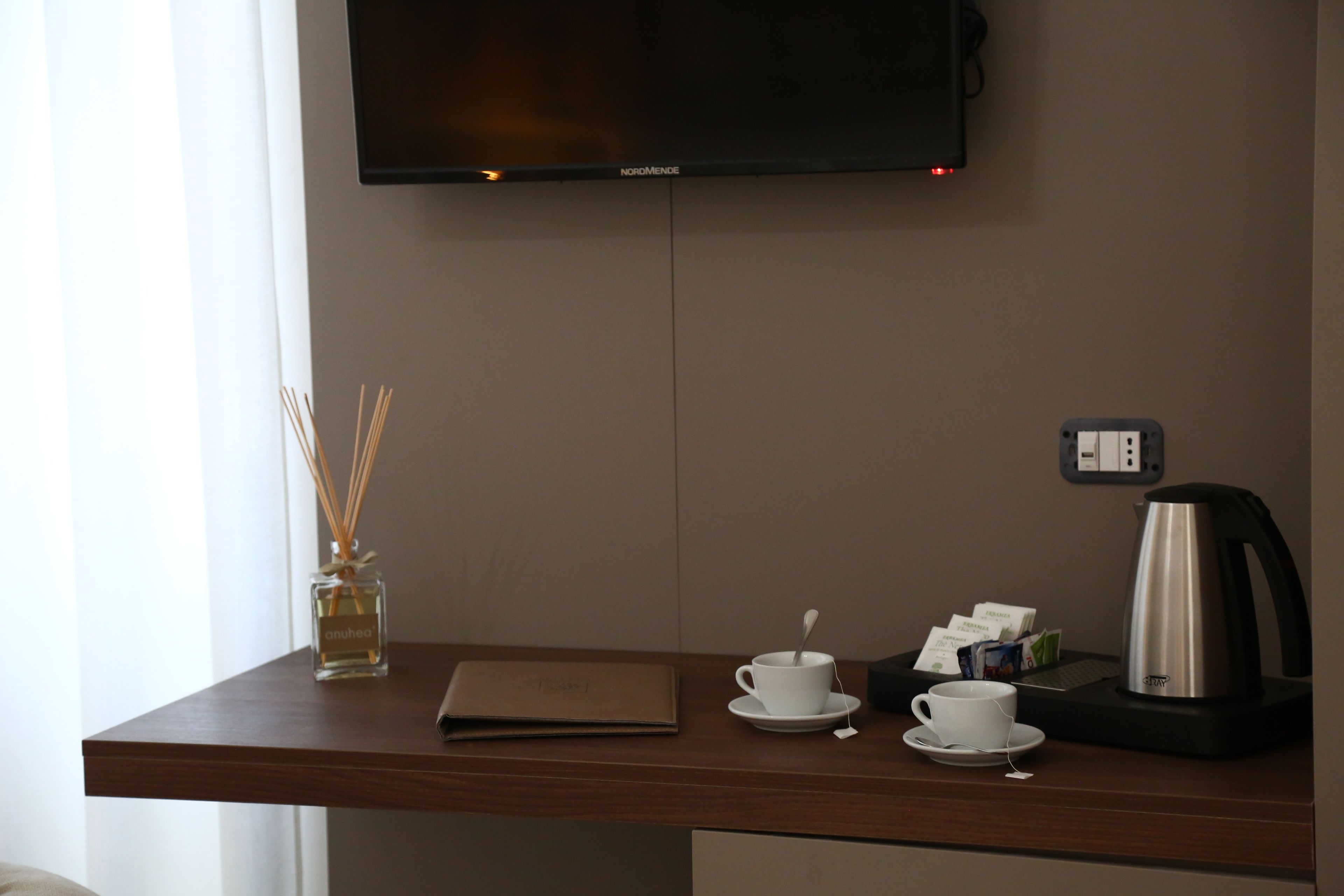 Ein Hotelzimmer mit Holztisch, Wand-Fernseher, Minibar und einem fenster mit Vorhängen.