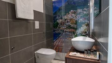 Une salle de bain moderne équipée d’un bidet, d’un grand lavabo et offrant une vue sur une ville côtière grâce à une porte vitrée.