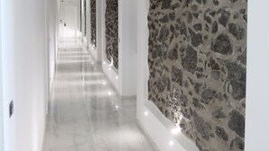 Un pasillo con piso de mármol, paredes blancas y una pared de piedra en un lateral.
