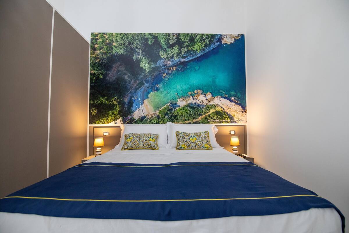 A hotel room with a large bed, a view of a coastal landscape, and two bedside lamps.