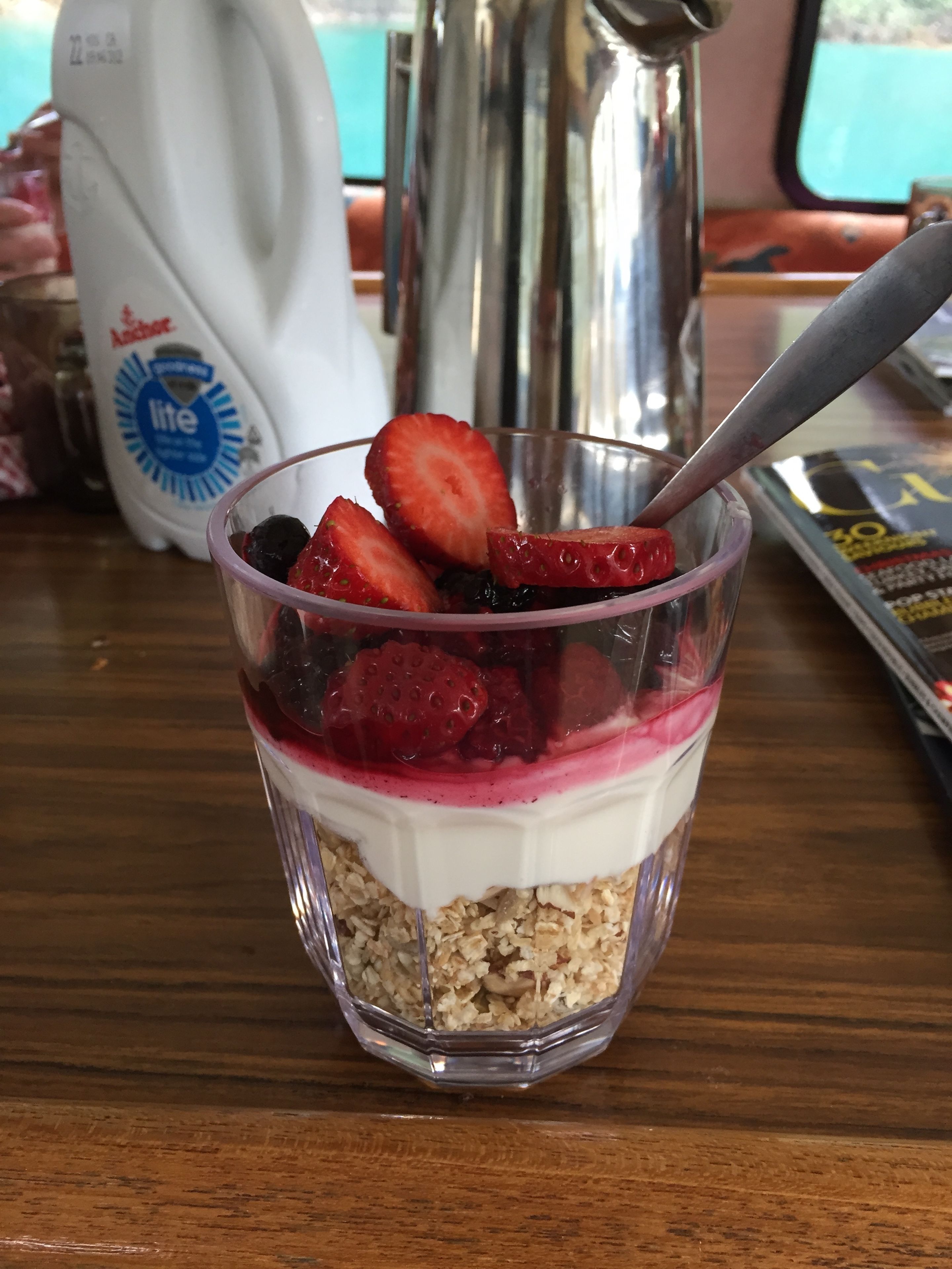 En genomskinlig glasskål som innehåller en dessert i lager med jordgubbar och ett vitt, krämigt lager, placerad på ett träbord.
